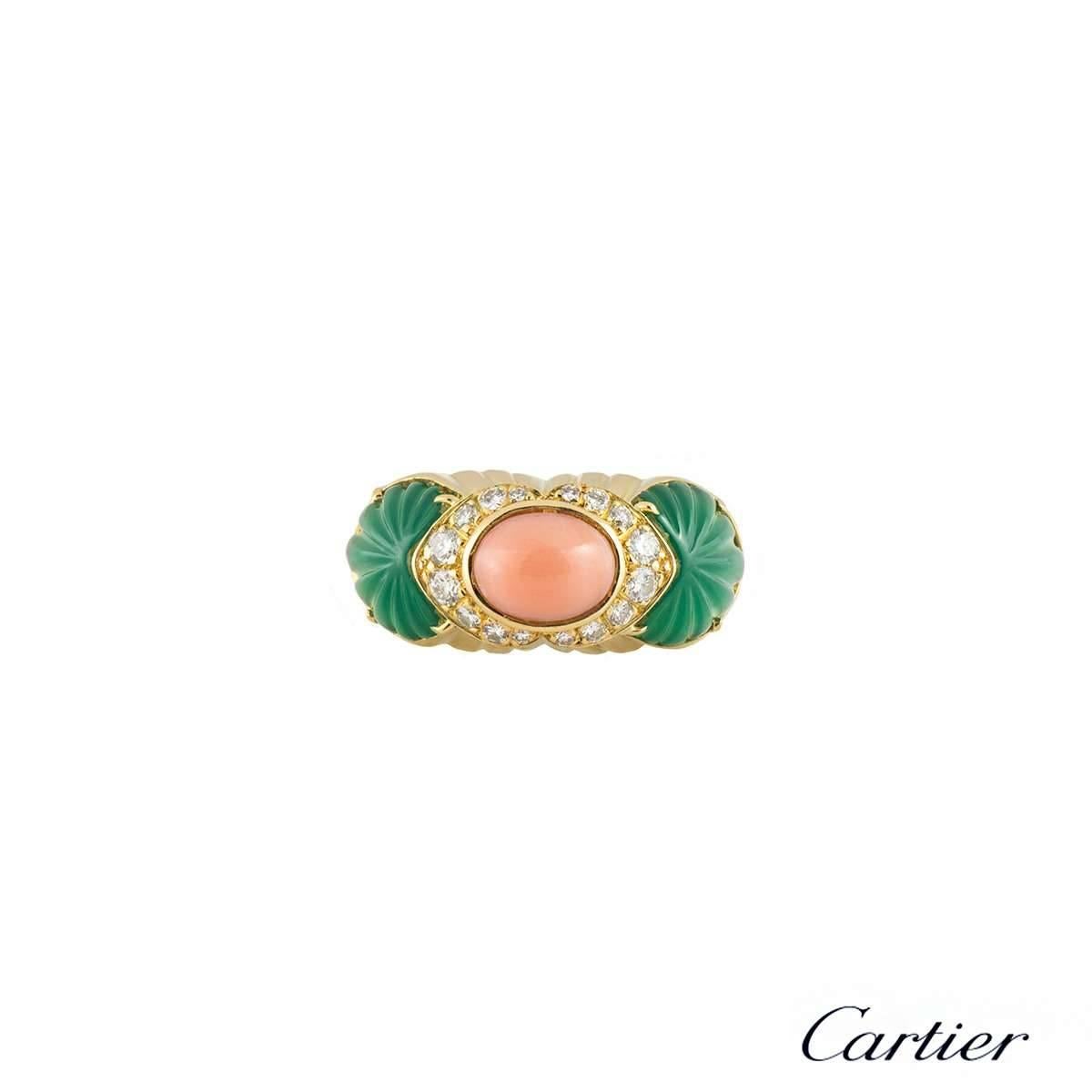 An 18k yellow gold dress ring by Cartier. The ring is set to the centre with a cabochon cut coral with a surround of 16 round brilliant cut diamonds totalling approximately 0.40ct, G colour and VS clarity. Flanked on either side are 2 carved