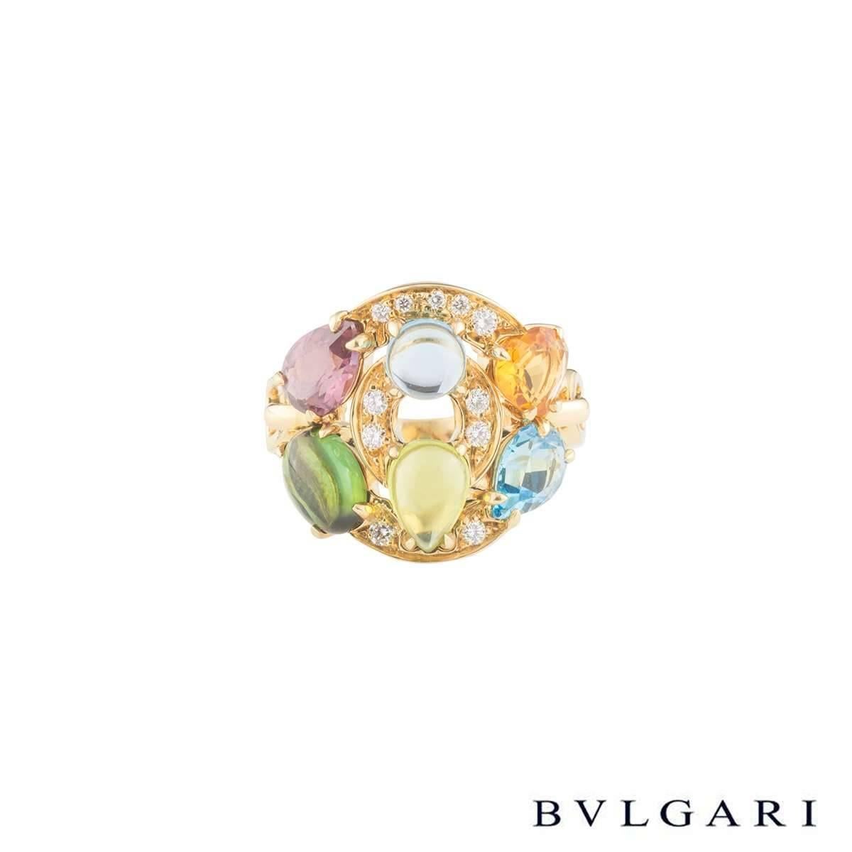 An 18k yellow gold Bvlgari multi-gemstone ring from the Astrale collection. The ring is composed of 2 graduating circular pave set diamond and multi-stone discs. The discs are composed of a variety of faceted and cabochon gemstones, including blue