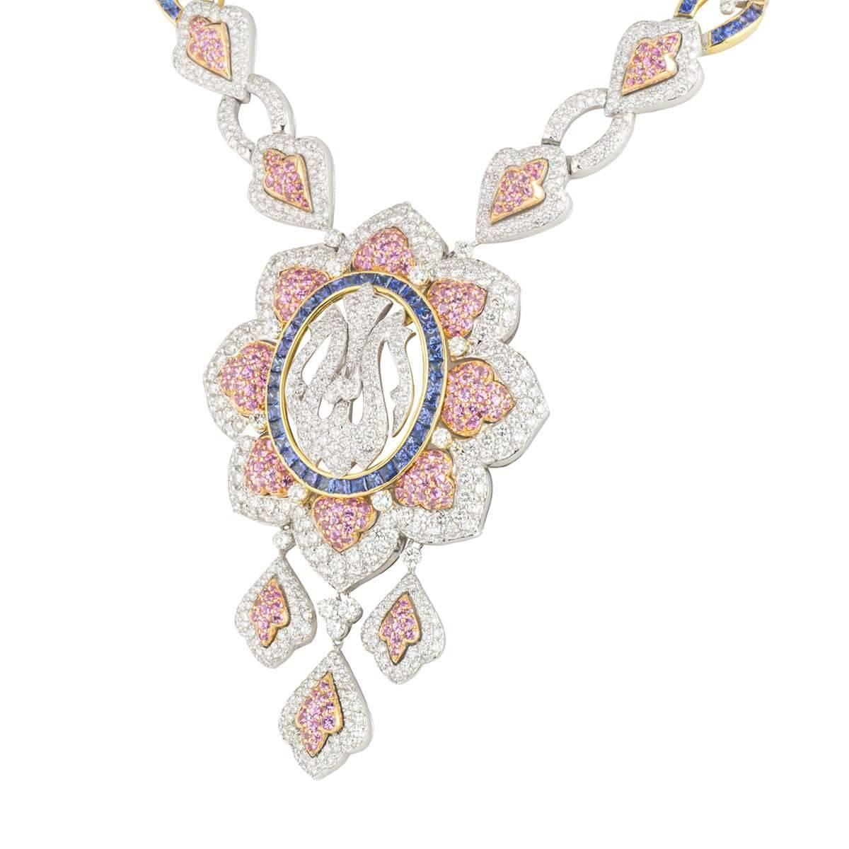 An exclusive 18k white and yellow gold diamond and multi-gemstone necklace. The necklace comprises of a circular motif with the 'Allah' written in arabic set with round brilliant cut diamonds. The motif has princess cut sapphires set in a yellow