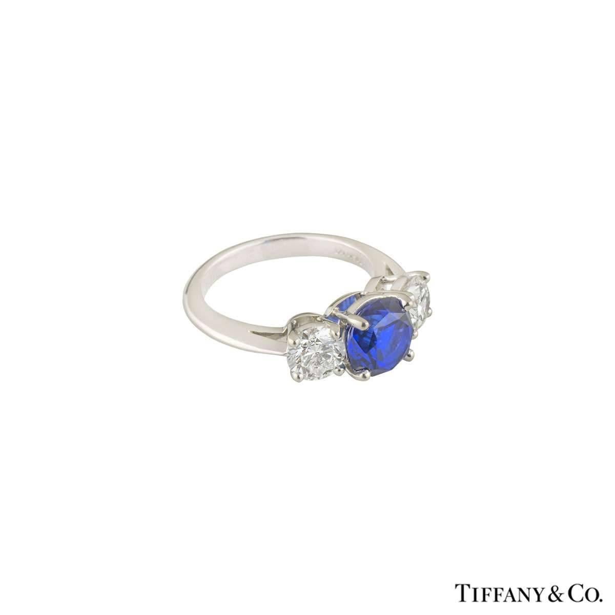 A luxurious platinum Tiffany & Co. diamond and sapphire ring from the Three Stone with Sapphire collection. The ring comprises of a round brilliant cut sapphire in a 4 claw setting in a platinum band. Complementing the centre diamond are 2 round