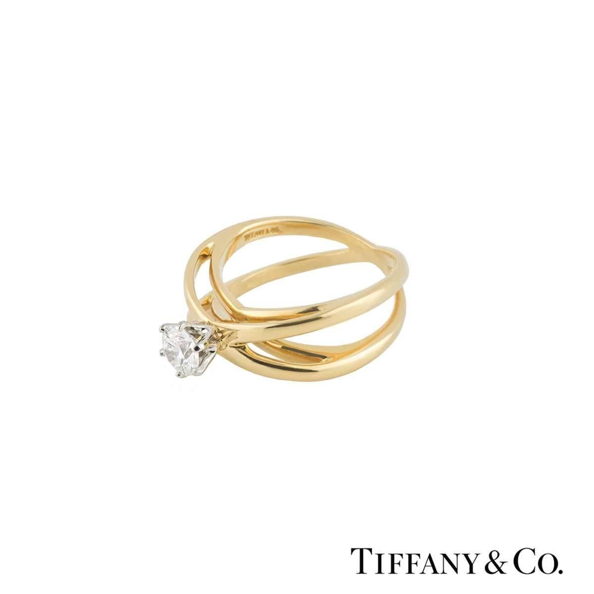 A lovely 18k yellow gold Tiffany & Co. diamond engagement ring. The ring comprises of a round brilliant cut diamond in a 6 claw with a total approximate weight of 0.40ct, F colour and VVS2 clarity. The ring has a crossover style band with a band