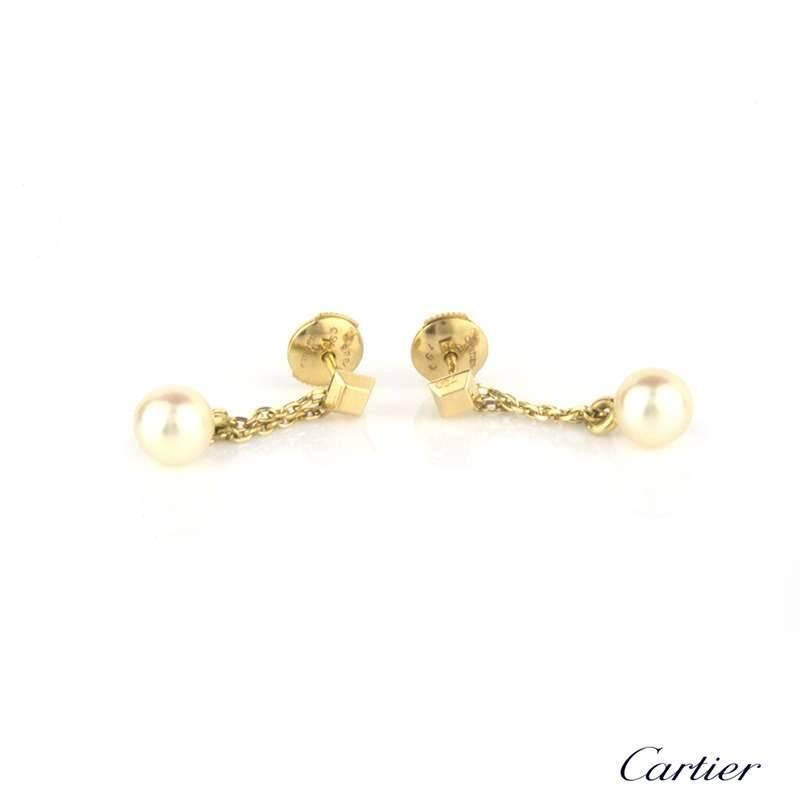 A pair of pearl drop earrings in 18k yellow gold by Cartier. The cube shape surmount suspends a trace chain leading to the cultured pearl. Each 6.8mm pearl has a cream body colour with a  pink tint. The pearls are in good condition. The earrings are