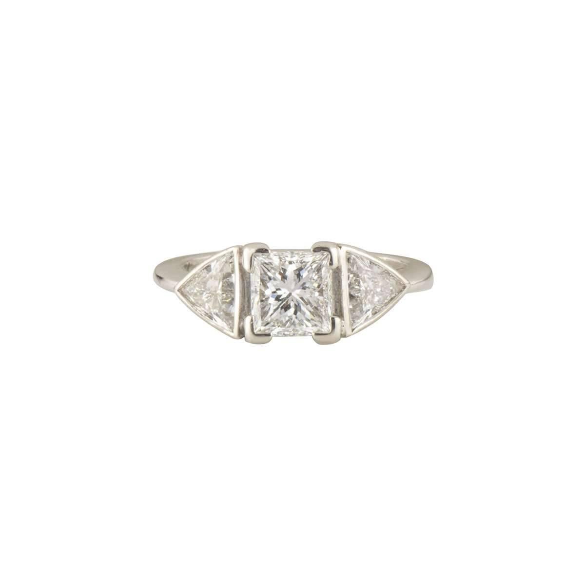An exquisite 18k white gold diamond ring. The ring comprises of a princess cut diamond with a weight of 1.07ct, predominantly D colour and VS2 clarity. Complementing the central diamond are two trillion cut diamonds set either side with an