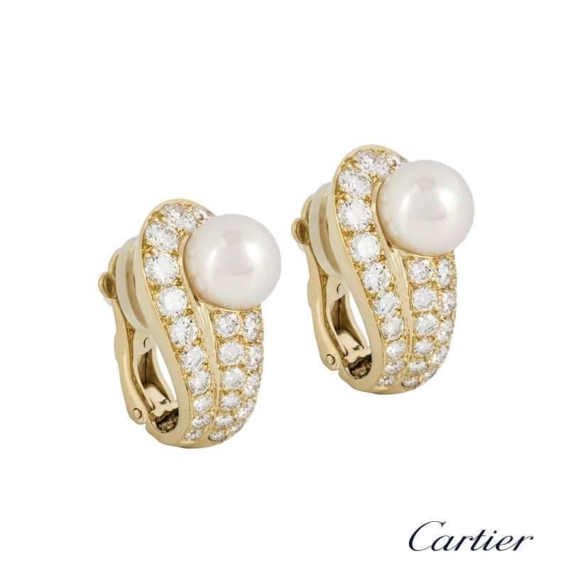 A pair of elegant 18k yellow gold diamond and pearl earrings by Cartier. The earrings are set to the centre with a round 8.3mm cultured pearl, of which disperses a mix of cream and pink lustre throughout. Accentuating the pearl are pave set, round