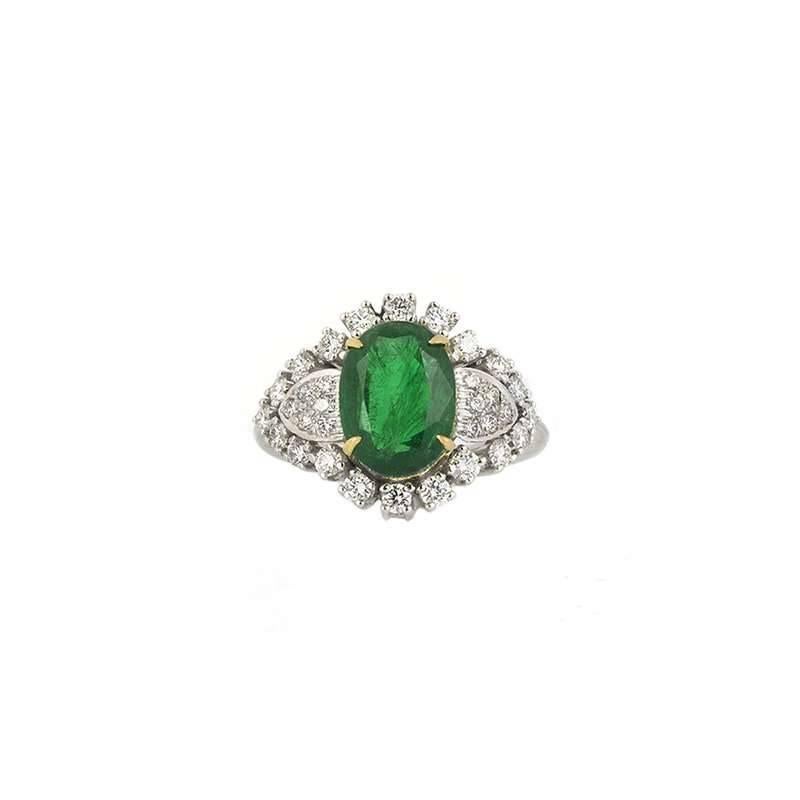An 18k white gold emerald and diamond dress ring. The ring is set to the centre with an oval cut emerald weighing approximately 2.80ct set within an 18k yellow gold 4 claw setting. Either side of the emerald sit 5 round brilliant cut pave set