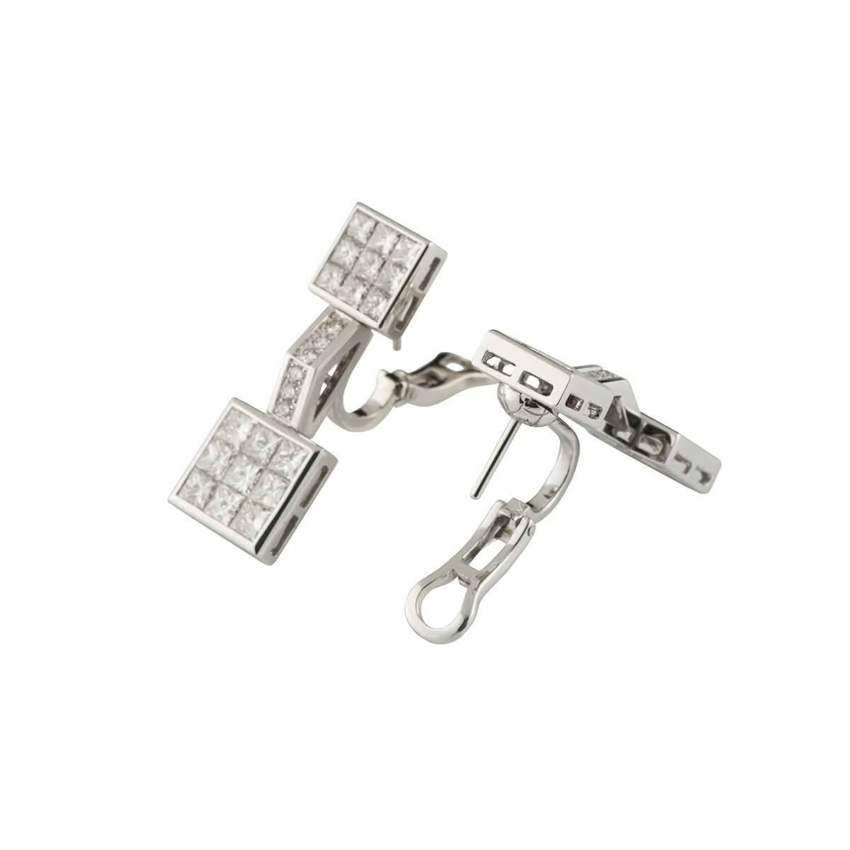 A sparkly pair of 18k white gold diamond earrings by Mouawad. Each earring comprise of 2 square motifs with a bar connecting the two. The square motifs have 9 princess cut diamonds in each and the bar features 6 round brilliant cut diamonds in a