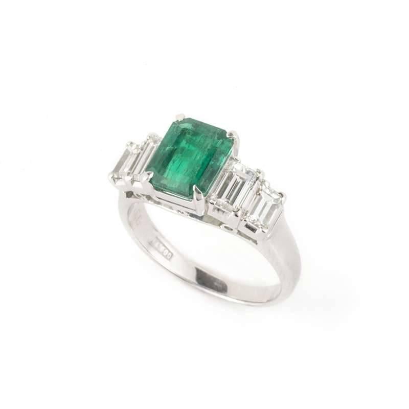 A stunning emerald and diamond ring set in 18k white gold. The art deco design inspired ring is set to the centre with a stunning claw set 1.66ct emerald. On either side step set baguette cut diamonds accentuate the emerald. The total diamond weight