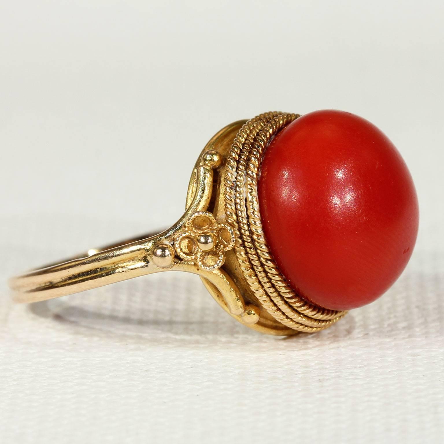 This rare antique Victorian Etruscan Revival style red coral button ring was handcrafted around 1870. It is circled thrice around with twisted golden wirework and accented with golden beads. The large lozenge of coral measures 12 mm in diameter.