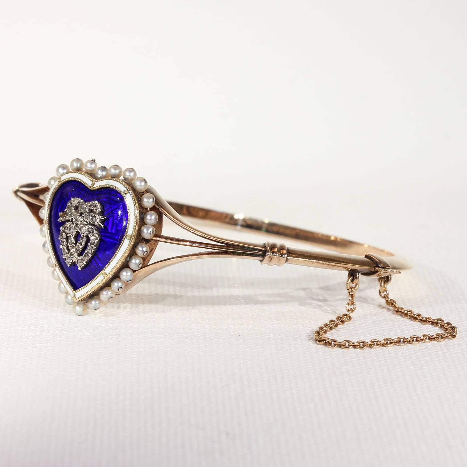 Set in a halo of 26 pearls, the face of this bangle features a blue enamel heart with a white edging. The heart is set with interlocking twin hearts topped with a bow, these are crafted in silver and set with tiny rose cut diamonds. However, this