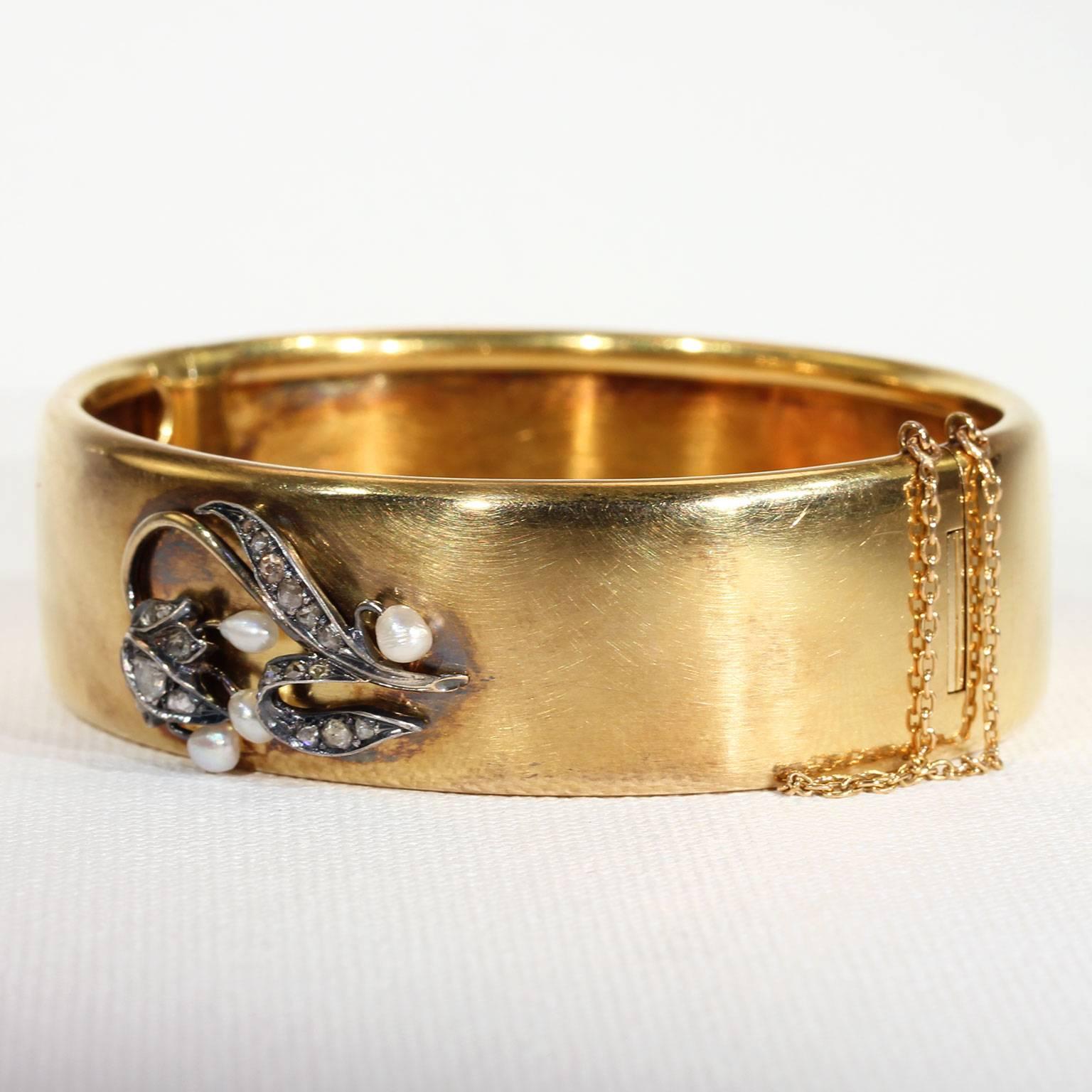 This darling antique Victorian gold bangle features a lily of the valley flower made up of diamonds and pearls. It was handcrafted in about 1870 and has a safety chain for added security. The sparkling lily featured on this bangle is made up of 20