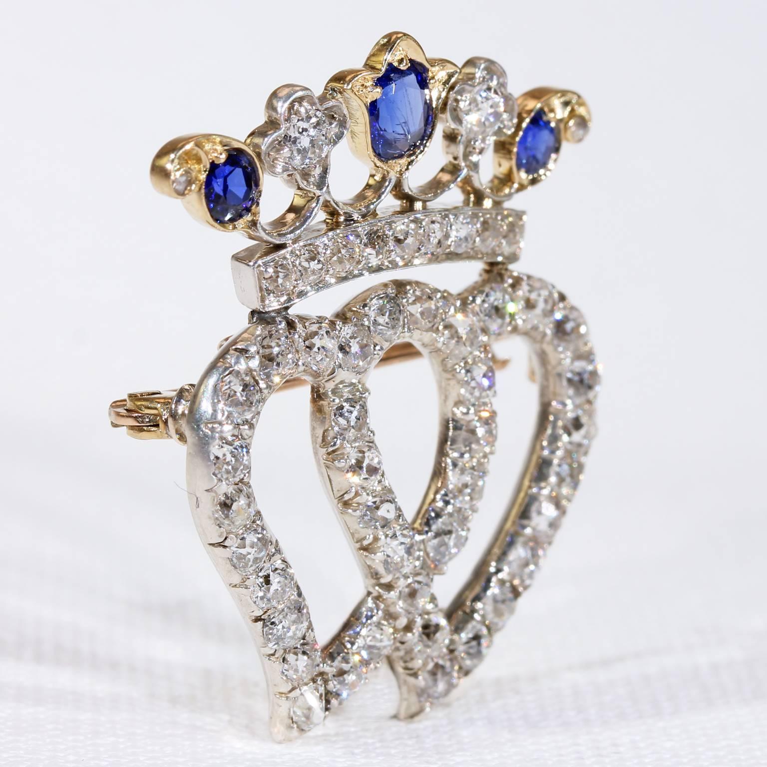 This antique Victorian sapphire and diamond heart brooch-pendant was handcrafted in England, around 1860 by the famed company of Edward Tessier. It features a double heart motif, topped with a crown of diamonds and sapphires. The stones are set in