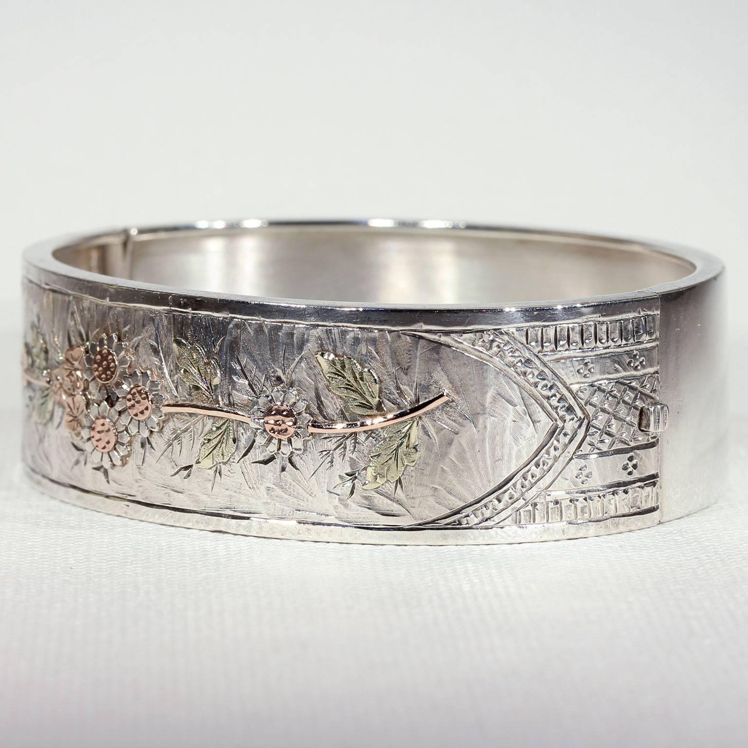 This stunning antique Victorian silver bangle was handcrafted in Birmingham, England, in 1882. It features a fully worked flower motif with rose colored stems and petals, as well as perfectly green leaves. It’s engraved with tiny squares and