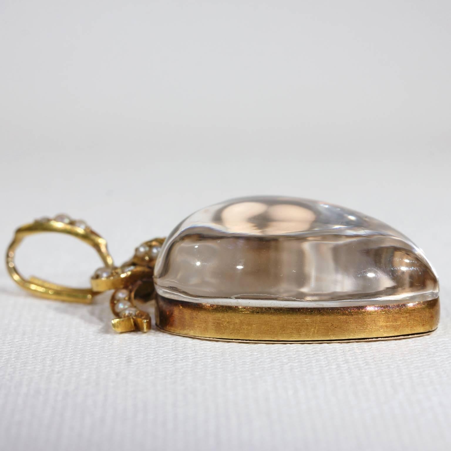 This fabulously large antique Victorian crystal locket pendant was handcrafted in England, around 1870. It features a deep heart shaped rock crystal set in 15 karat gold, with a golden bow on top, decorated with 20 white lustrous pearls. The