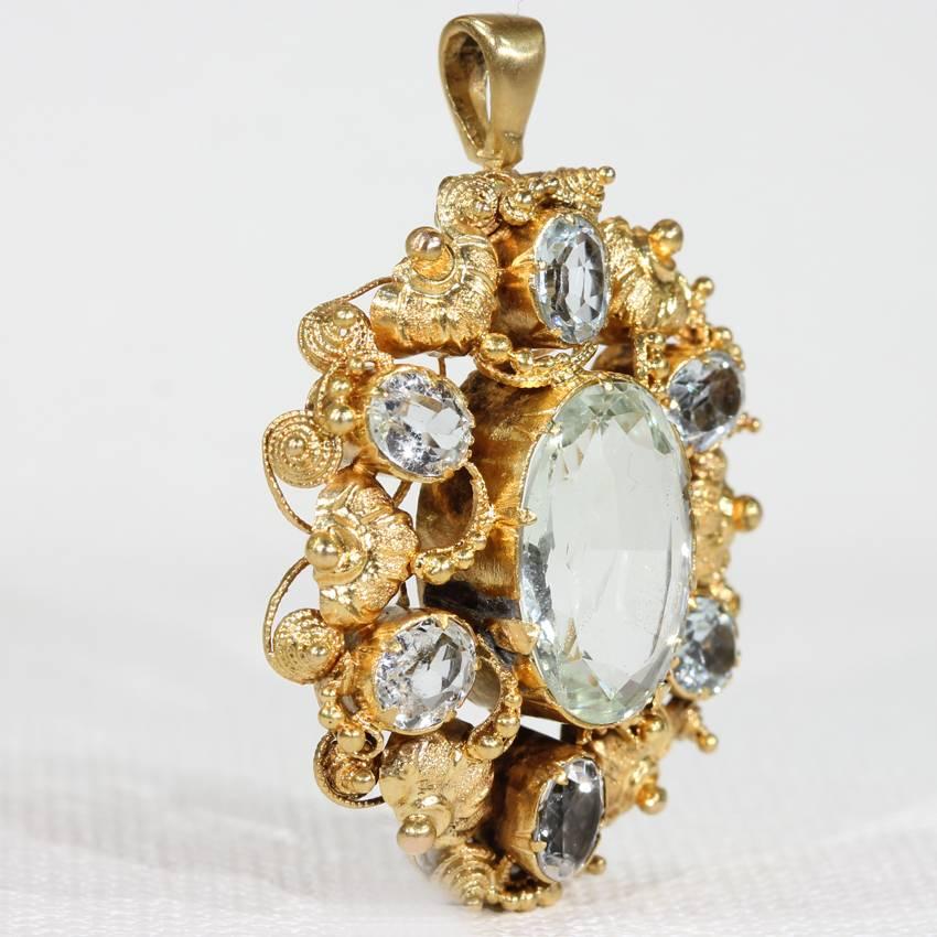 This antique early Victorian aquamarine and gold pendant was handcrafted around 1850, in England. There are seven light blue colored oval faceted aquamarine stones set in 15 karat gold. The design is graceful and gold. It swirls as it creates