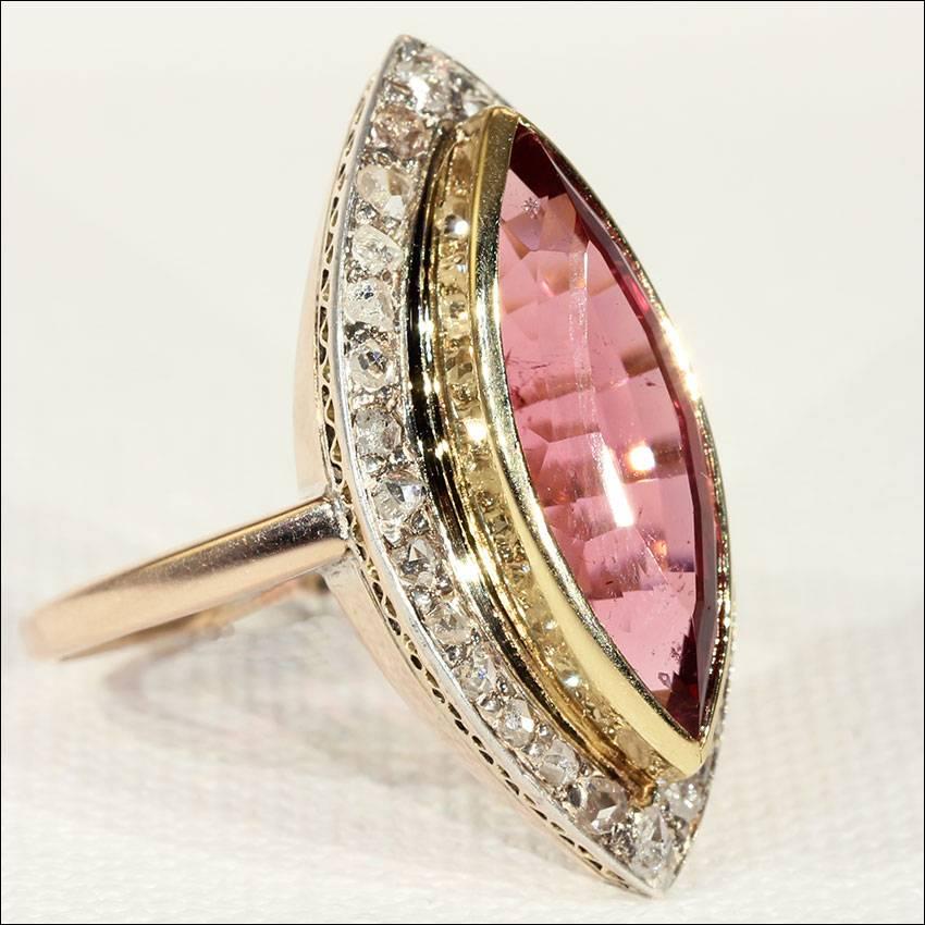 This stunning tourmaline and diamond navette shaped gold ring features a pink marquise cut tourmaline stone, measuring 20.6 x 7.9 x 7.2 mm and weighing approximately 6.10 carats The juicy deep pink stone is bezel set in 14 karat gold. Surrounding