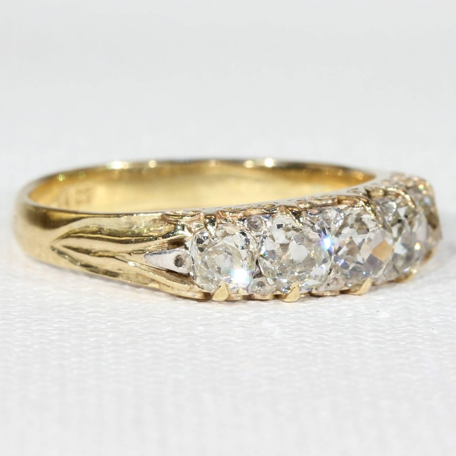 This antique Victorian diamond and gold ring was handcrafted in England around 1890. This glimmering English ring features five Old European cut diamonds, totaling approximately 1.2 carats. These round precious stones are lined in a row, and set in