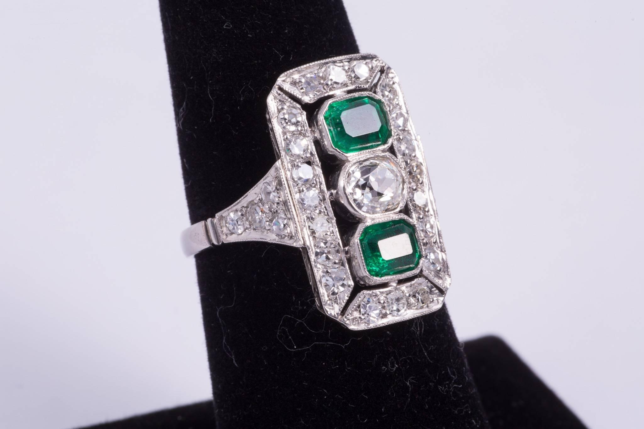 Emerald and diamond ring with two emeralds that weigh approx. 1.00cts total. The emeralds have wonderful rich green color. The diamond in the center is an approx. .50ct antique cushion cut diamond and has G-H color and VS2-SI1 clarity. There are 28