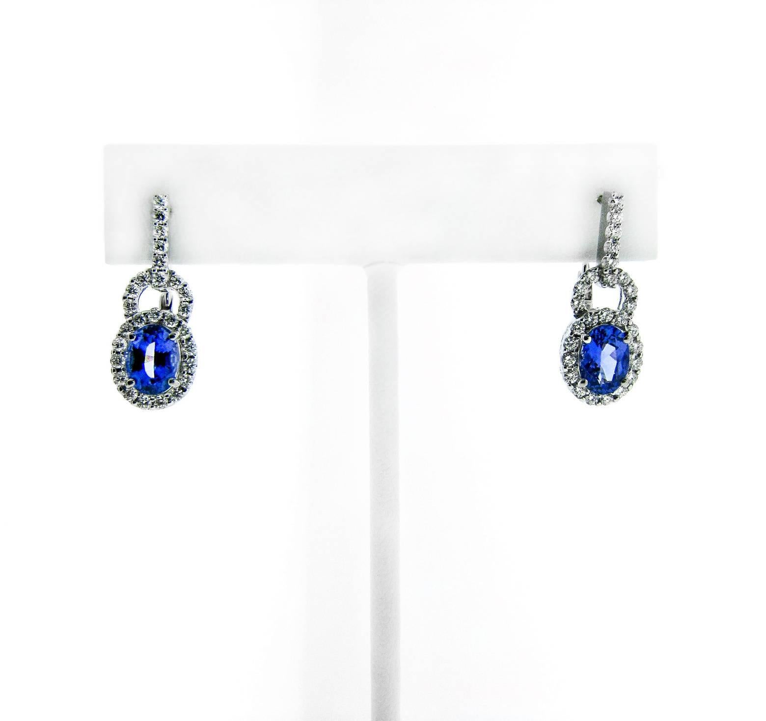 These elegant 18 karat white gold earrings feature shimmering oval faceted blue Tanzanite gemstones (2.86 carats). Luminous white diamonds surround the center stone, create a beautiful arc above it, and travel up the length of the earrings. These