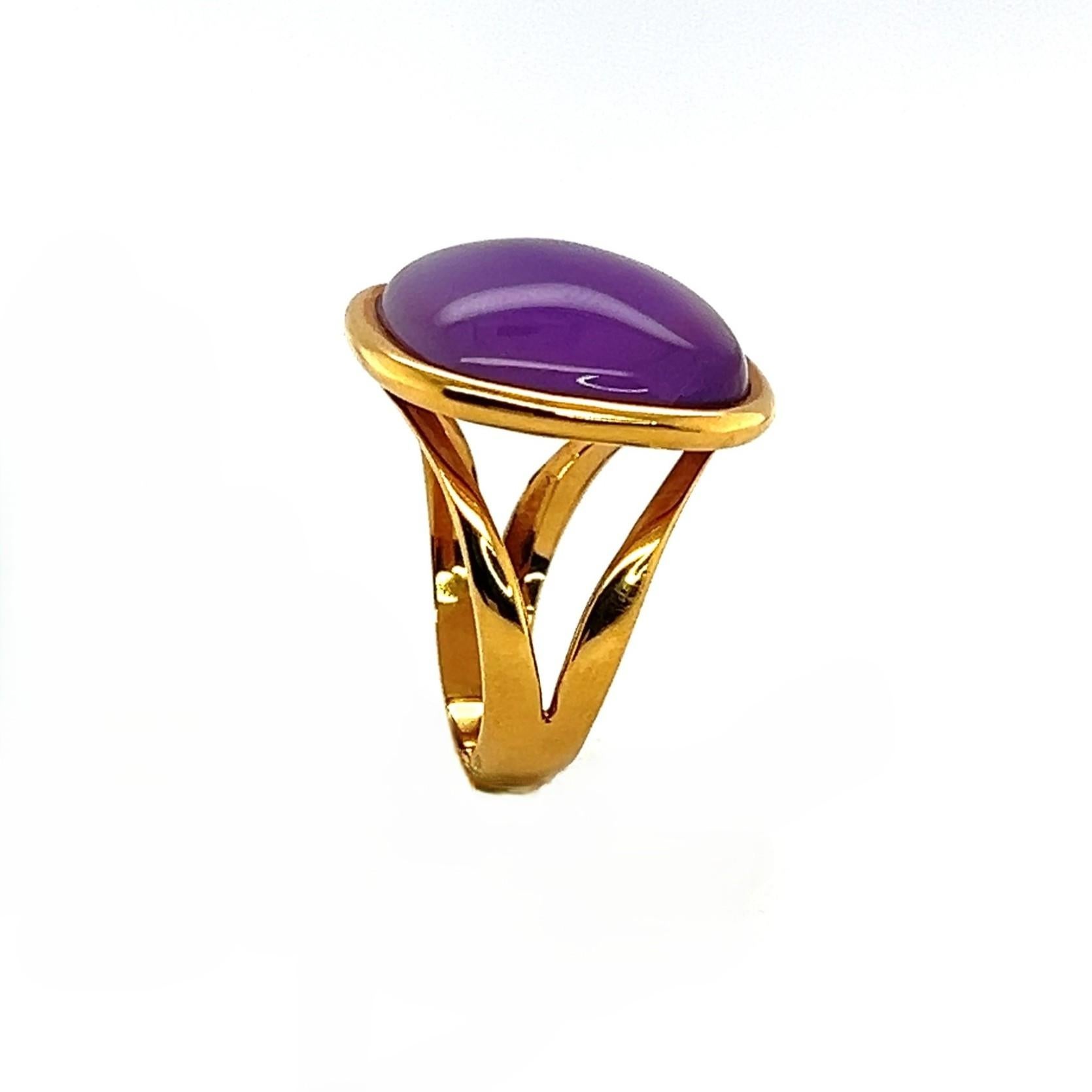 Questo anello elegante e distintivo presenta uno splendido cabochon di ametista a cupola con sottili riflessi iridescenti che ricordano la madreperla. La gemma è incastonata in un ricco oro giallo da 18 carati, creando un contrasto morbido ma