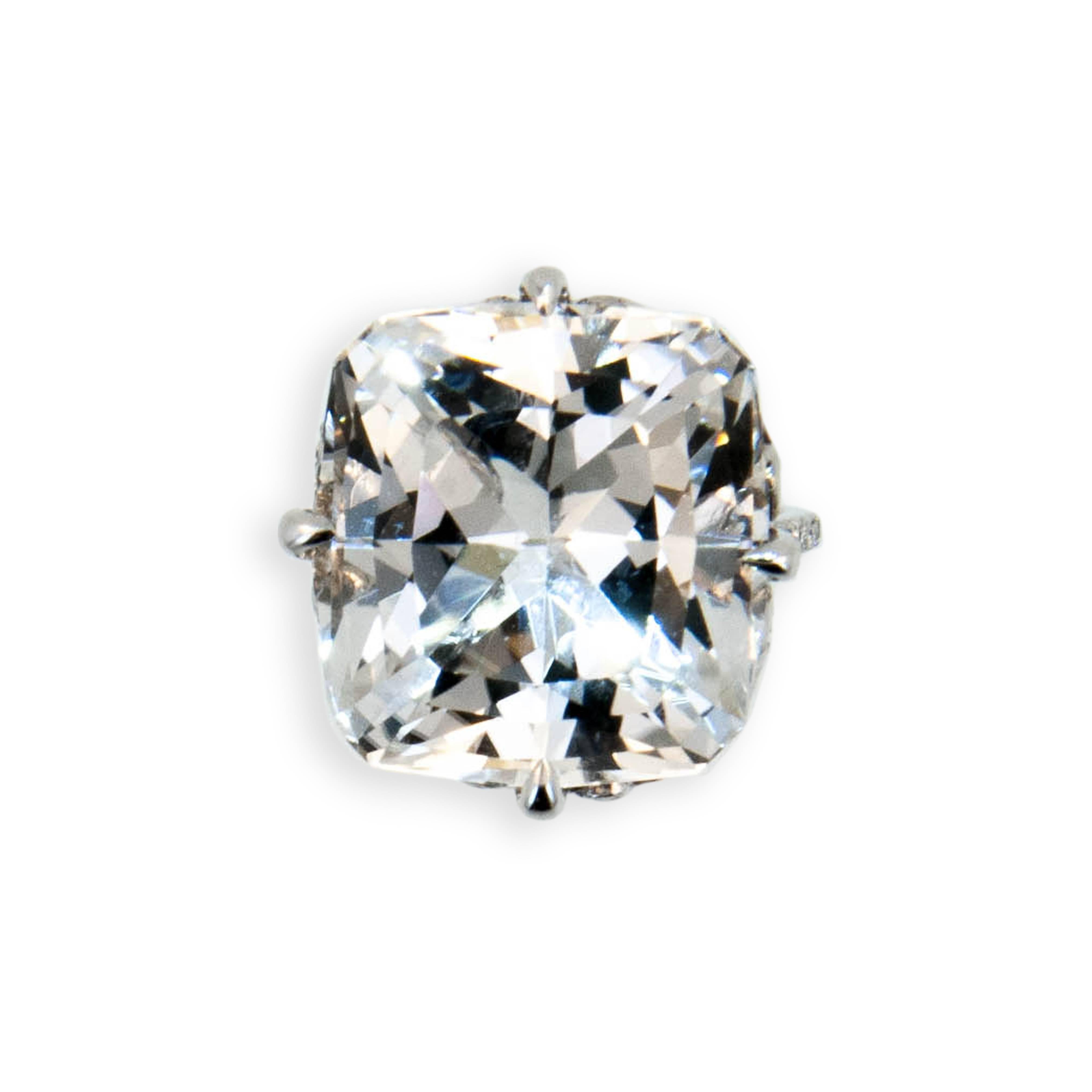 18 karat white gold ring set with one faceted pillow cut Topaz very light grey color 27.99 carats. Flower motif on sides of basket set with (4) round Blue Sapphires .32 carat total weight. Basket prongs and 1.6 mm shank are set with 104 round
