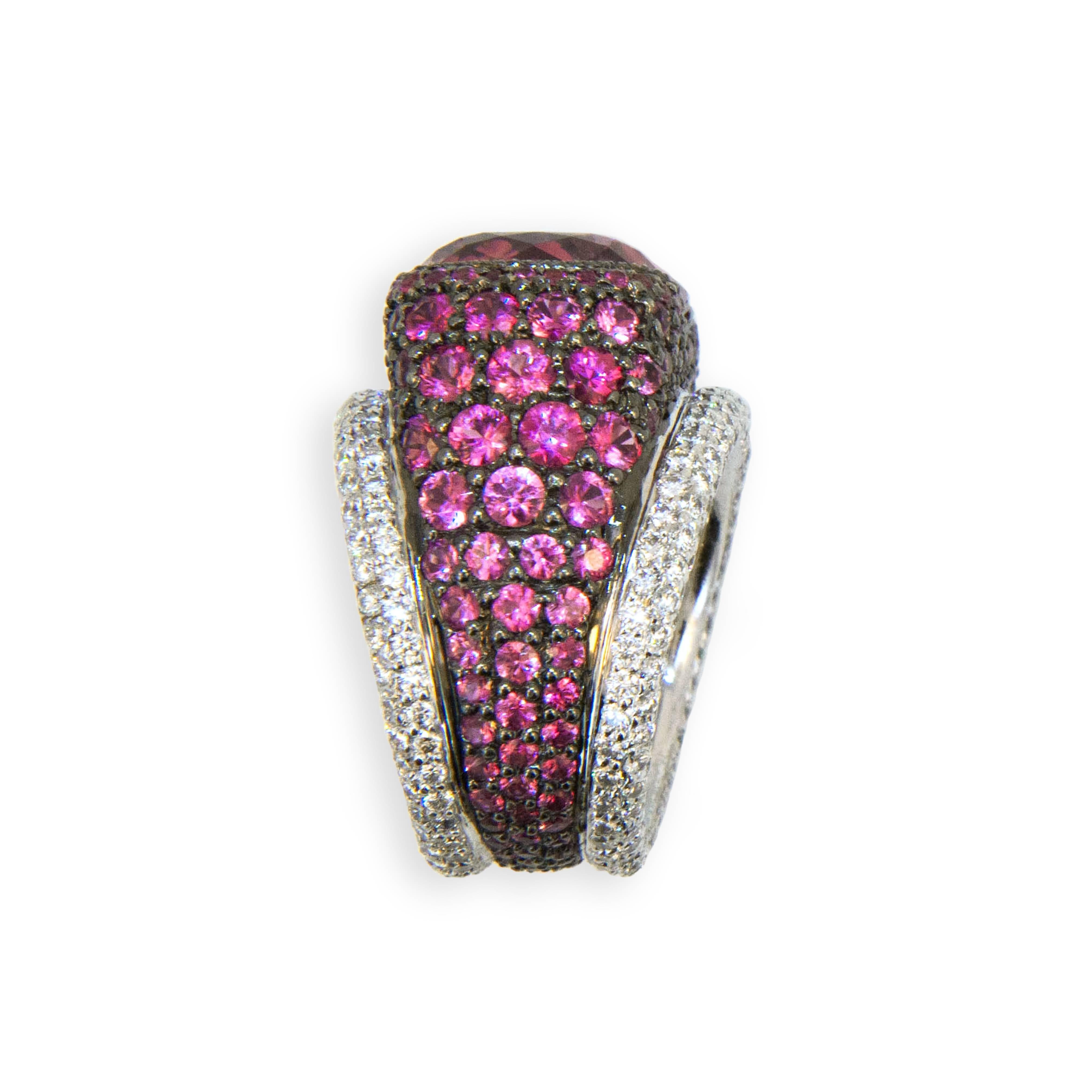 18 karat blackened white gold ring set with a cushion cut Pink tourmaline 12.65 carats total weight 14.68 x 13.72 x 9.36 mm, Surrounded by graduated cut and colored Pink Sapphires 5.86 carats total weight with two rows of diamonds 2.83 carats total