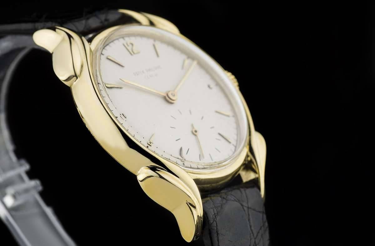 A 1950s 18k Yellow Gold Rare Flame Lugs Calatrava Wristwatch, silvered dial with applied 18k yellow gold hour markers and arabic 12, small seconds at 6 o'clock, an 18k yellow gold fixed polished bezel, an original black leather strap with a gold