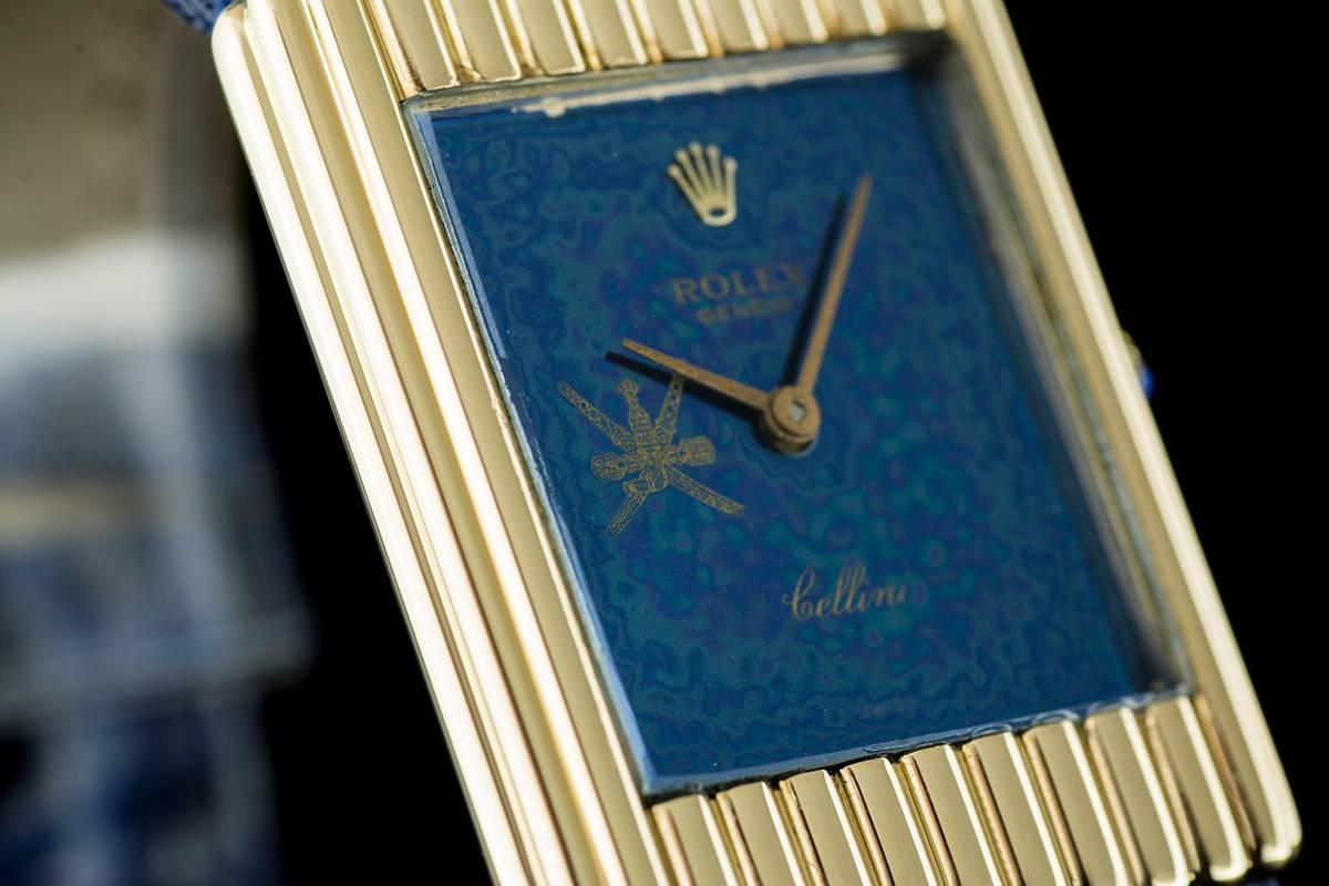 An 18k Yellow Gold Cellini Gents Wristwatch, blue "Omani Crest" dial, an 18k yellow gold cylindrical link style bezel, a blue leather strap with a gold plated pin buckle (not by Rolex), mineral glass, manual wind movement, in excellent