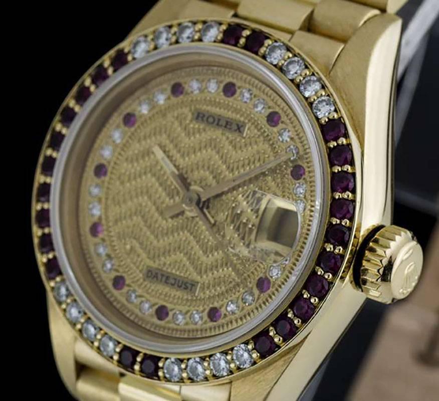 An 18k Yellow Gold Oyster Perpetual Datejust Ladies Wristwatch, rare champagne decorated string dial set with 22 round brilliant diamonds and 11 rubies, date at 3 0'clock, a fixed 18k yellow gold bezel set with 24 rubies and 16 round brilliant