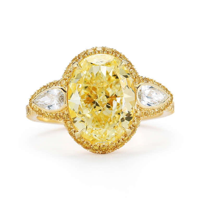 Prong-set with an oval-cut fancy light yellow diamond with yellow diamond trim and flanked on each side by a pear-shaped diamond, weighing approximately 0.76 carats and are F-G color, VS clarity. Accompanied by a Kwiat box.