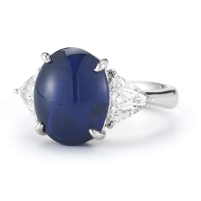 A beautiful, oval cabochon, no heat, Burmese star sapphire ring with trilliant-cut diamond shoulders set in platinum. This deep blue sapphire weighs approximately 6.76 carats and is set in a classic four-prong basket setting. Ring size is 5.75, and