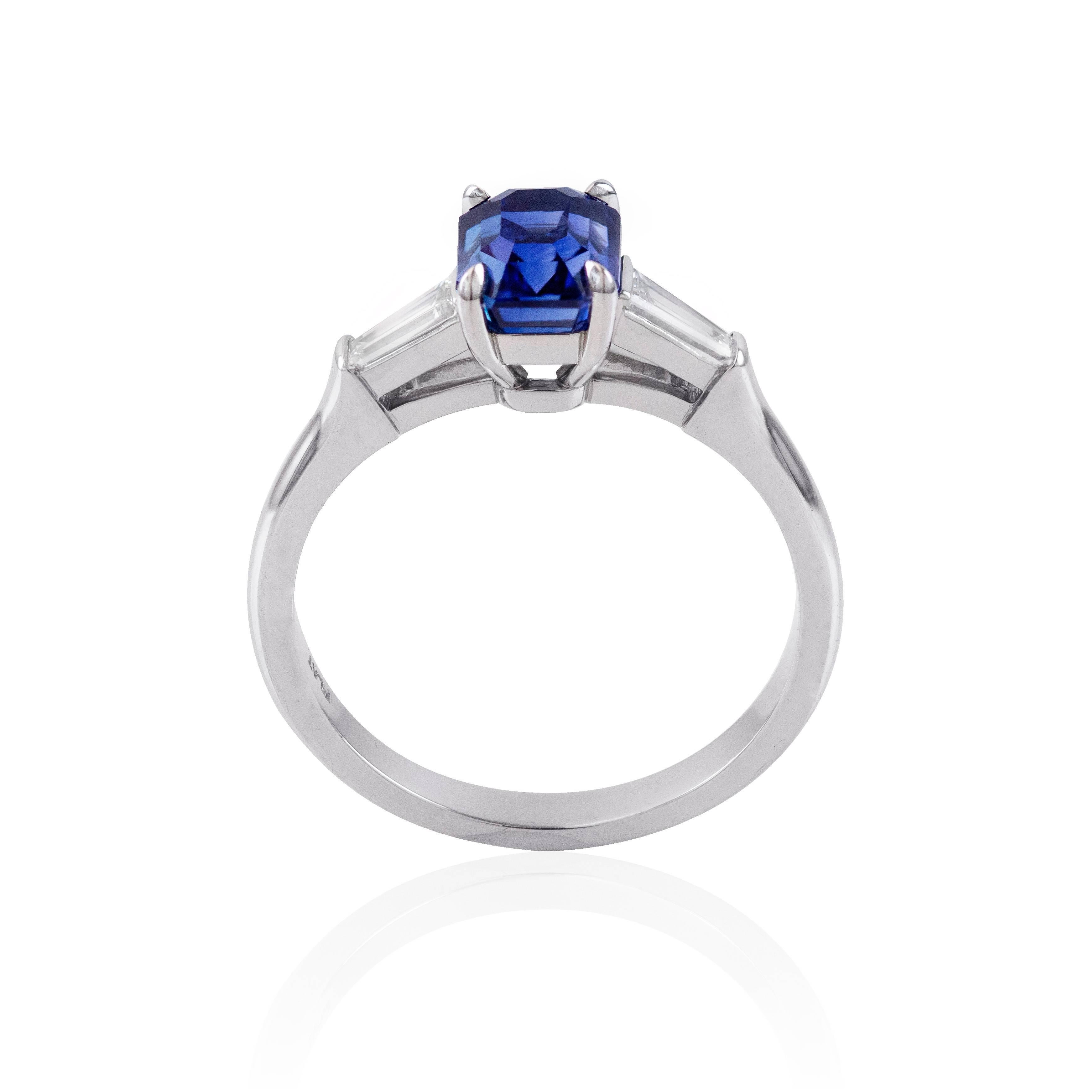 A timeless engagement ring, showcasing a 1.78 carats emerald cut blue sapphire with a deep royal blue color and clean eye, set on a four prong setting. Flanked by tapered baguette cut diamonds weighing 0.26 carat total. Finely made with a platinum