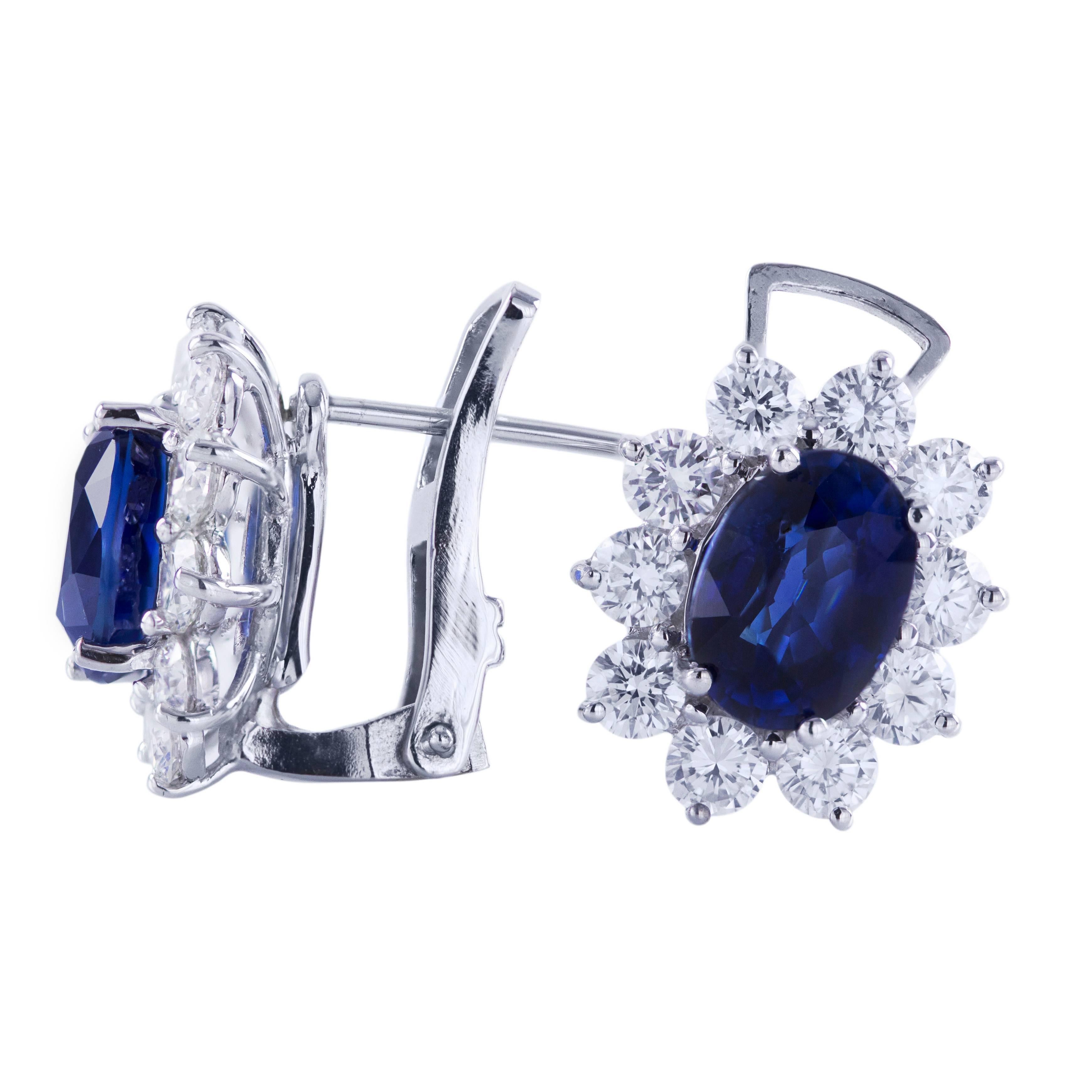 These beautiful cluster earrings feature 2 natural blue sapphire center stones. The weight of the sapphires is 3.96 carats total. Each sapphire is surrounded by a single row of round brilliant diamonds weighing 1.75 carats total. Latch back. Made in