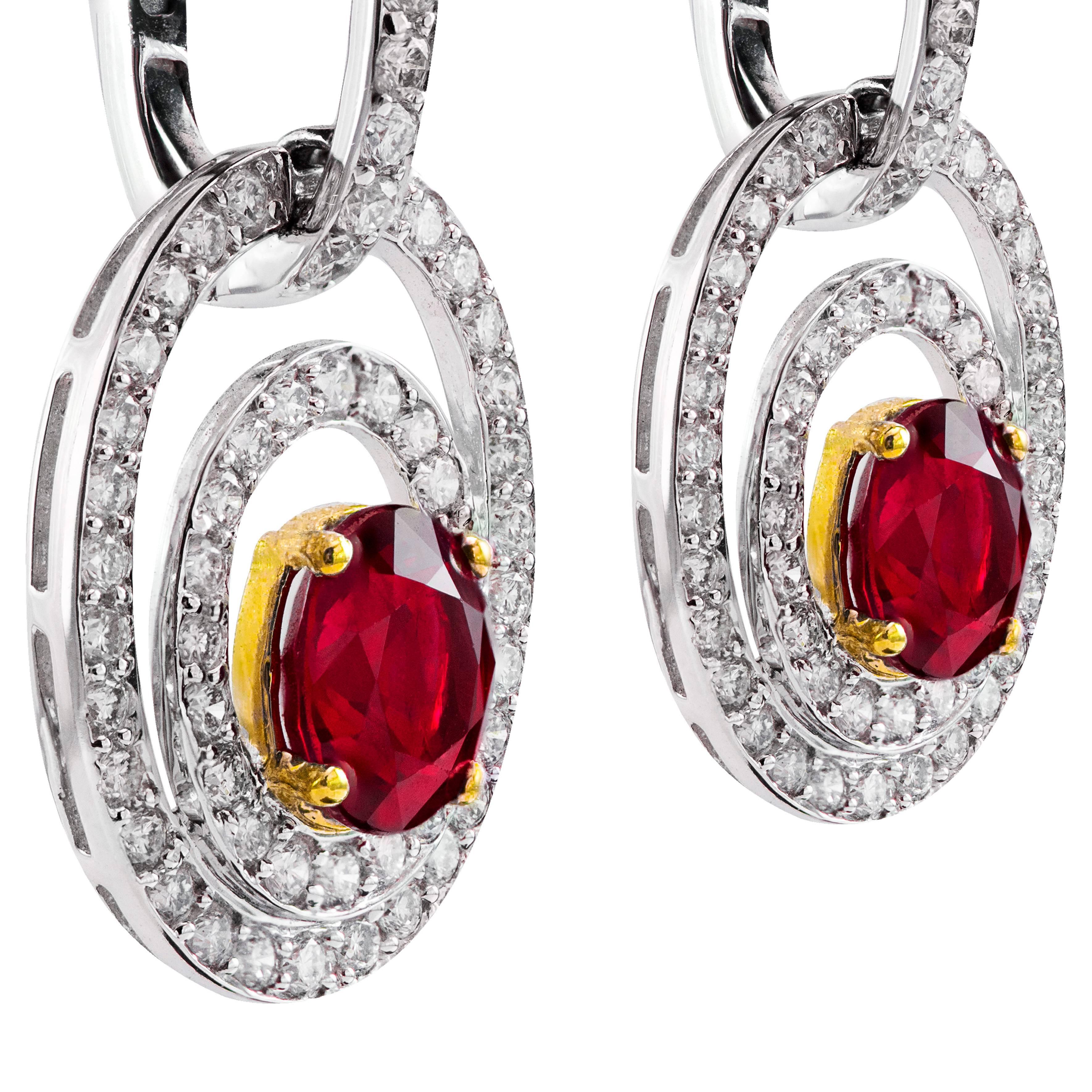 Estos pendientes colgantes brillantes y llenos de color presentan 2 rubíes talla oval con un peso total de 2,67 quilates, rodeados de 2 filas de diamantes redondos blancos brillantes en un diseño de halo abierto que se extiende hasta los aros con