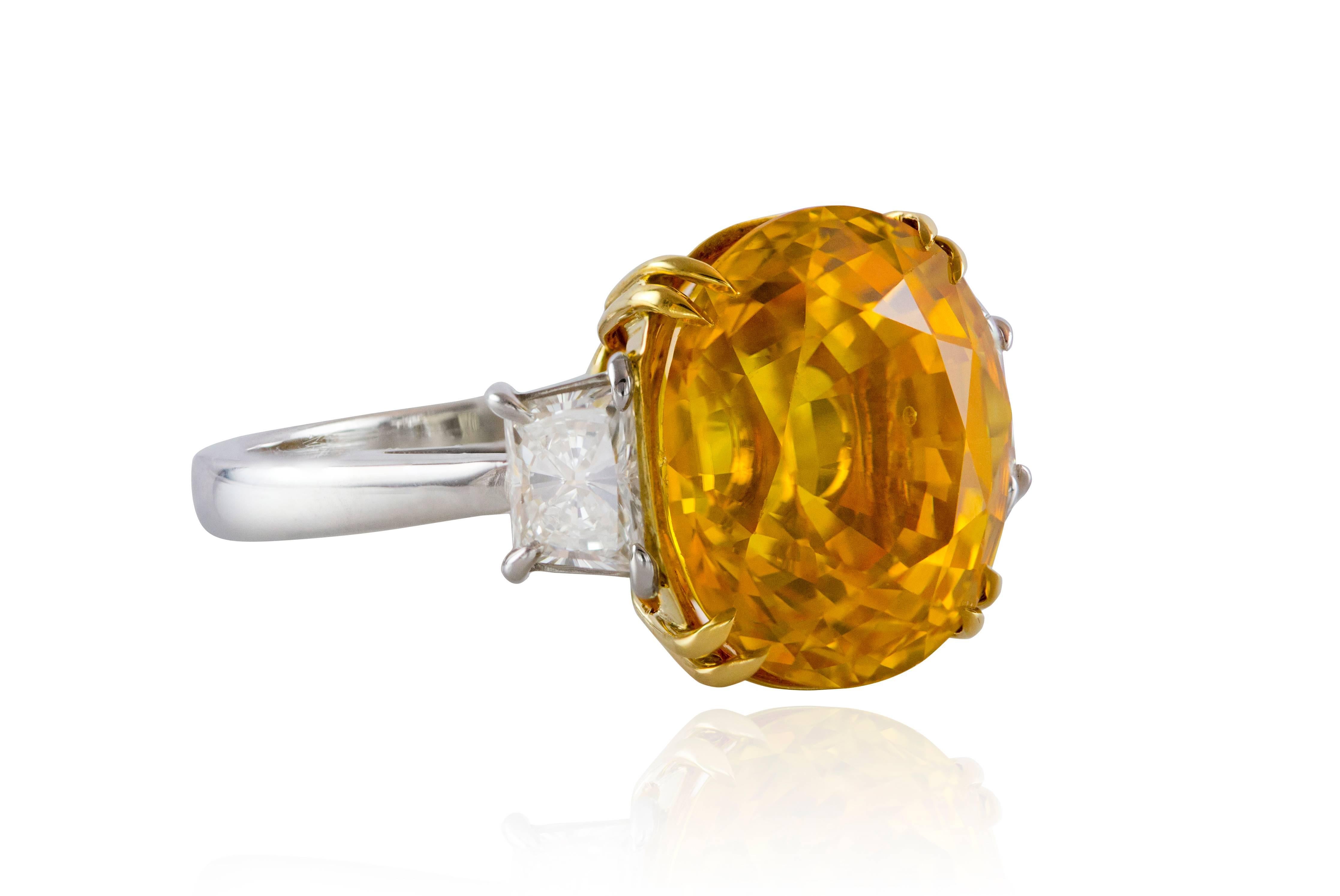 Features oval-shape natural yellow sapphire weighing 12.28 carat. The sapphire is certified by GIA and has indications of heating. The sapphire accented by trapezoid diamond on either side. Total diamond weigh 0.95 carat. The ring made of platinum
