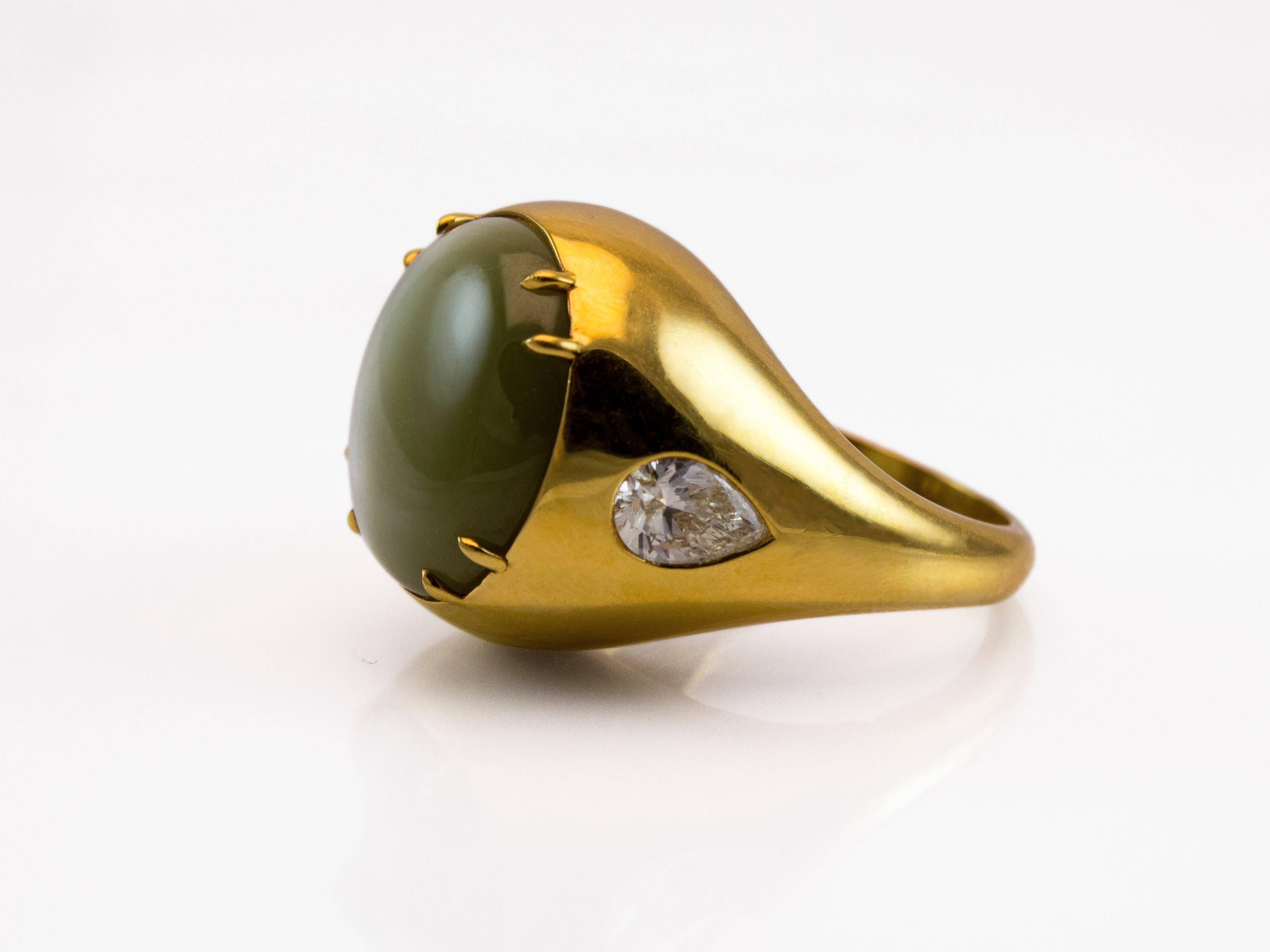 This cocktail ring features very rare large oval cabochon cat's eye chrysoberyl weighing 28.30 carat safely set in four prong 18K yellow gold. Accented by a pear shape diamond on either side weighing 1.03 carats total. The ring size is 8.25 US and