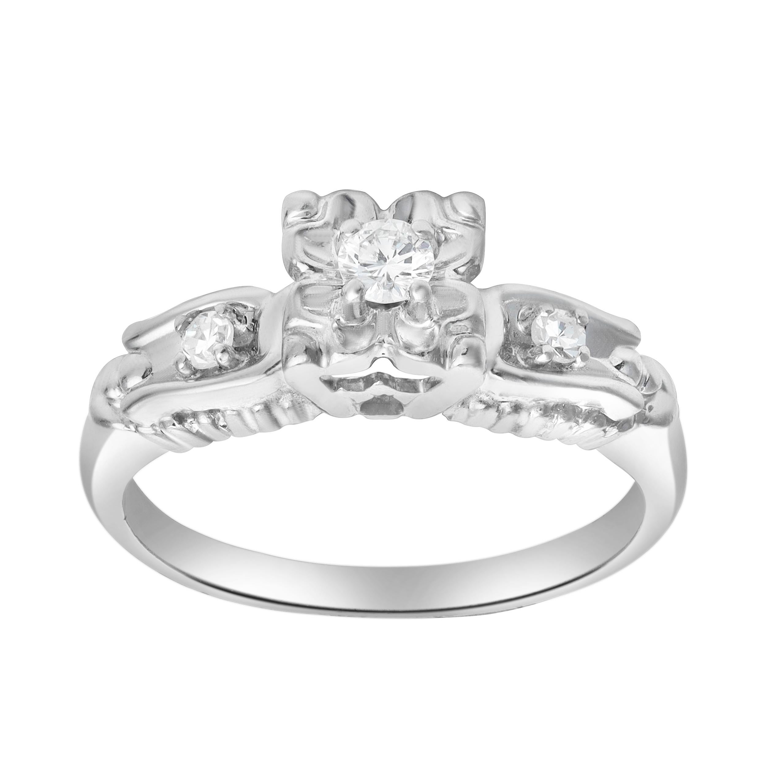Un meraviglioso anello di fidanzamento in stile antico, con tre diamanti rotondi taglio brillante del peso totale di 0,13 carati, ciascuno incastonato in una montatura a quattro punte. Il diamante centrale è accentuato da un bellissimo motivo