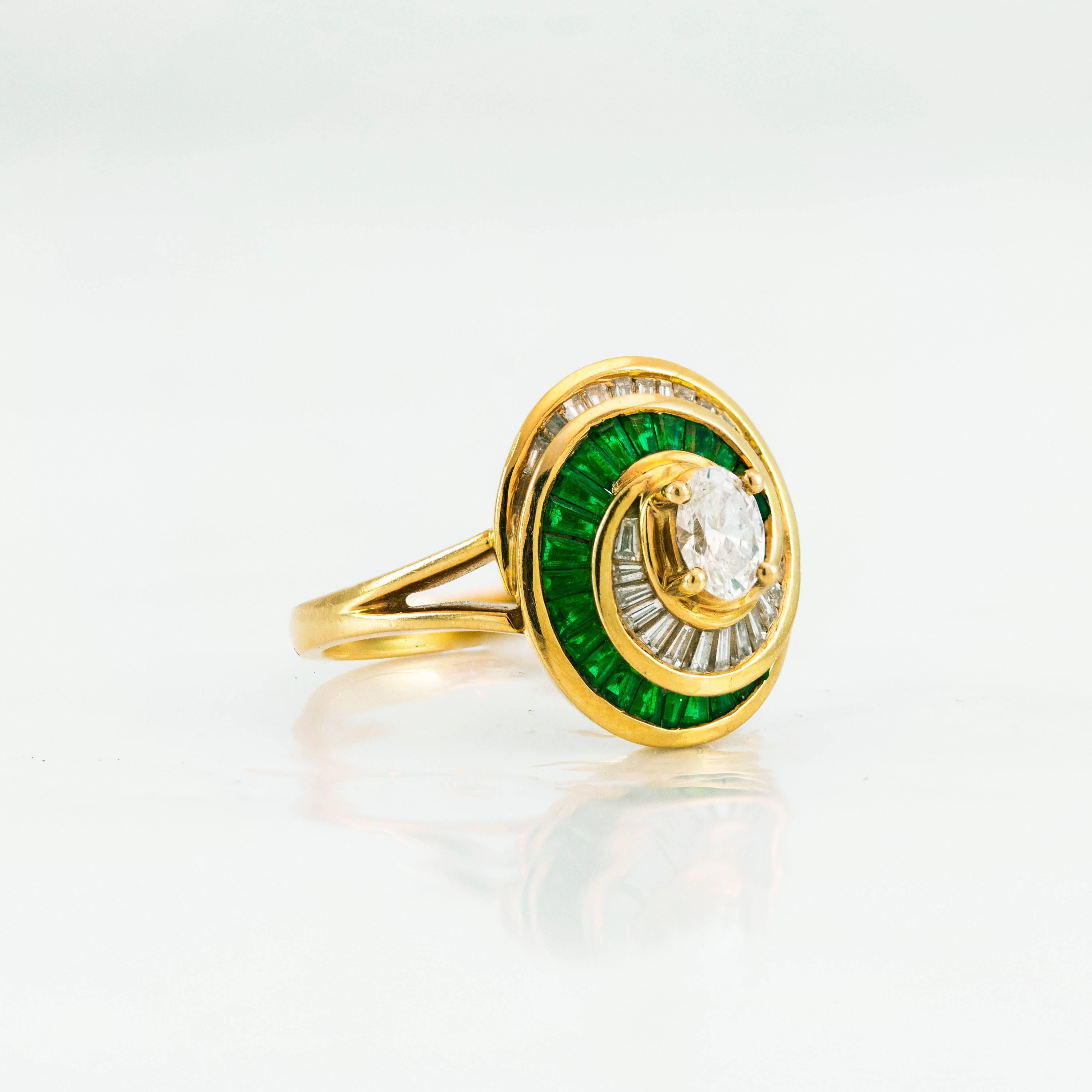 This gorgeous ring features a brilliant oval cut diamond center stone weighing 0.40 carats. The center stone is surrounded by emerald and diamond baguettes in a spiral design. Total weight of the emeralds and diamonds is 0.80 and 0.95 carats