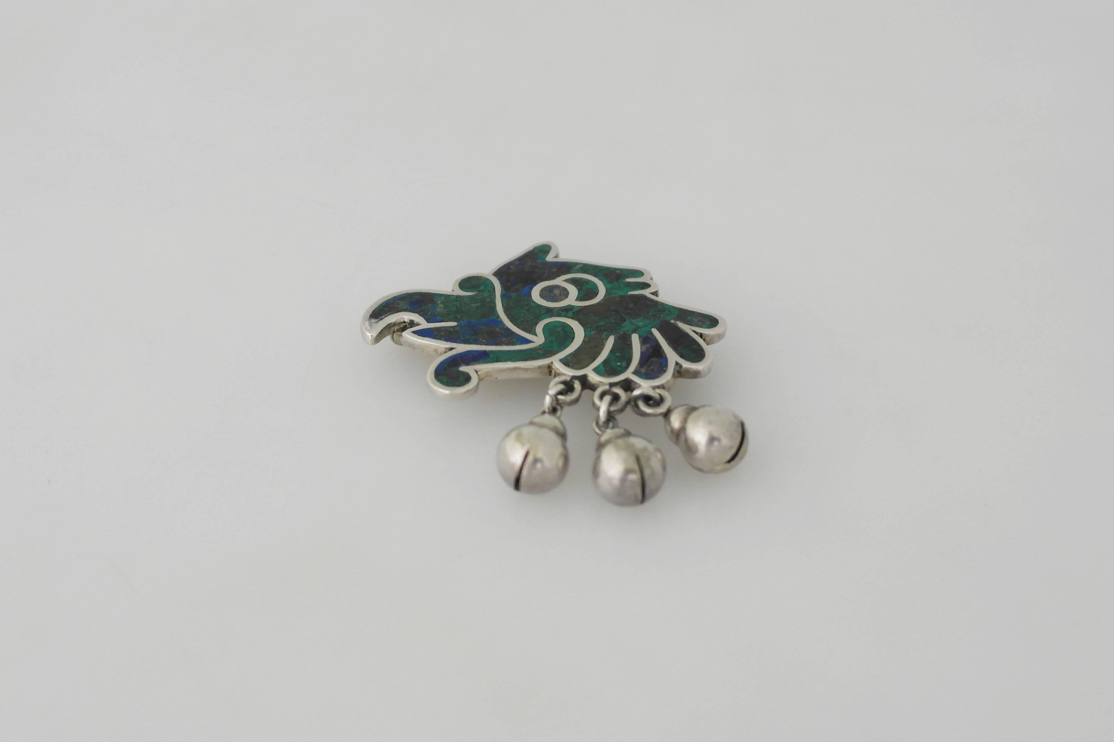 Being offered is a sterling silver brooch made by Los Castillo of Taxco, Mexico. Comprising a parrot motif with azur malachite stone inlay; three dangling bells. Dimensions: 1 1/2 inches x 1 3/4 inches. Marked as illustrated. In excellent condition.