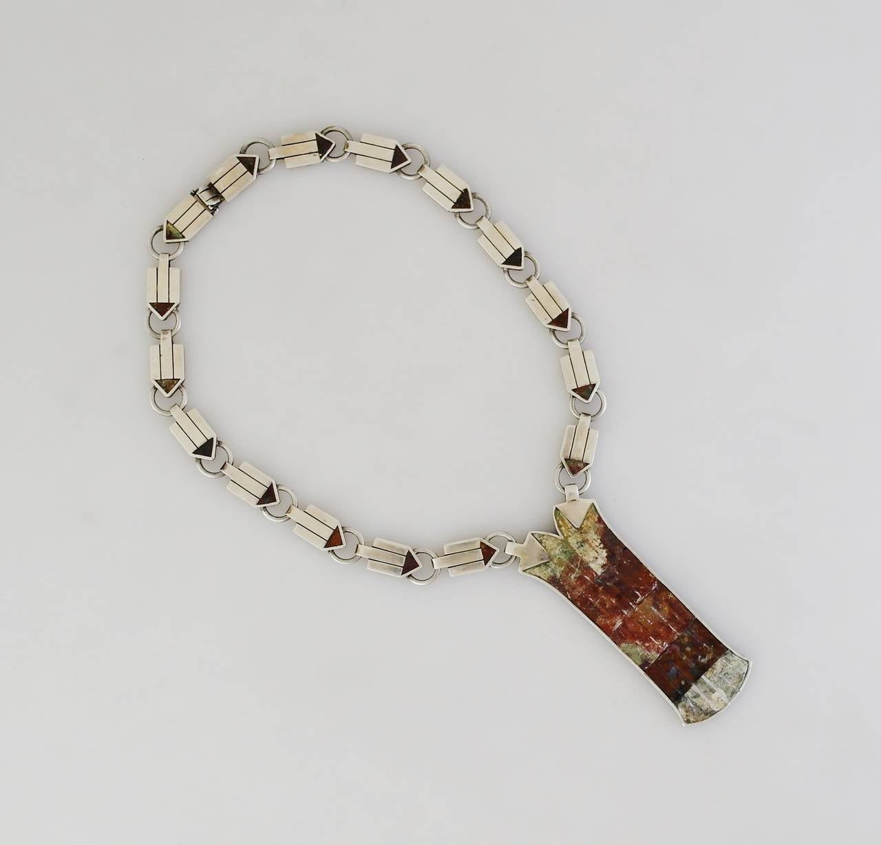 Being offered is a circa 1950 sterling silver necklace by William Spratling of Taxco, Mexico; rectangular links decorated with triangular hard stone insets, each connected with 'O' rings, supporting a large pendant with multi-stone inlay on both
