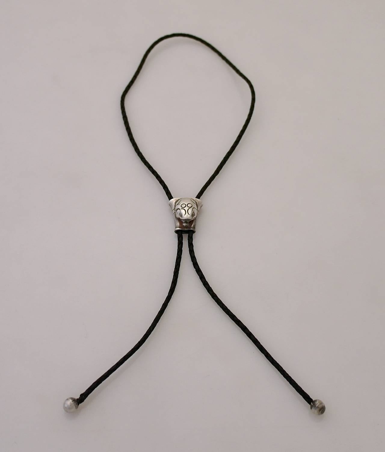 Being offered is a rare circa 1964 sterling silver and leather bolo tie designed by William Spratling of Taxco, Mexico, the woven leather tie (measuring 39 inches long) is supported by a hand made bolo accented by an applied frog motif with incised
