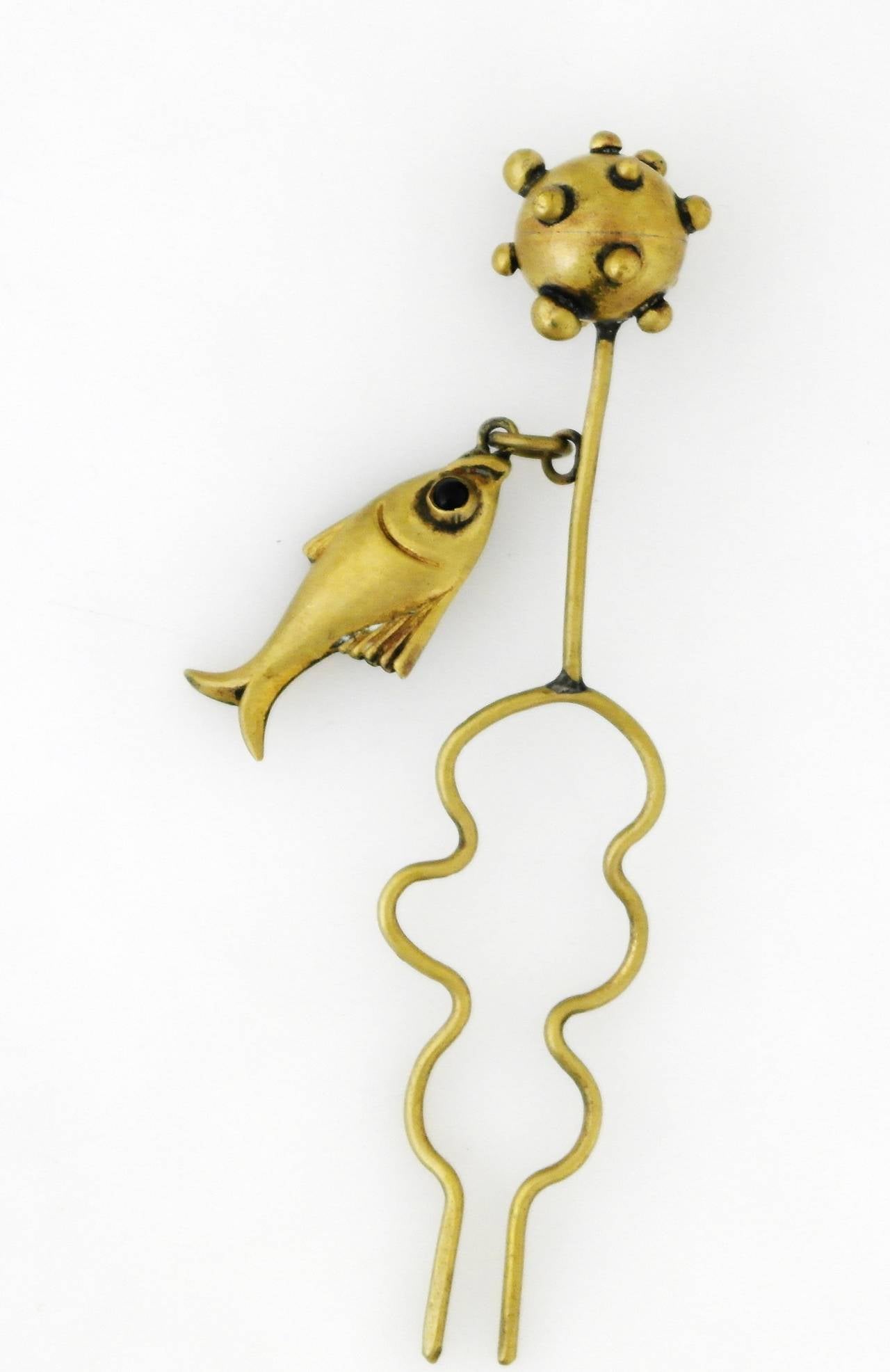 Being offered is a circa 1943 brass hair ornament by Hubert Harmon of Taxco, Mexico. Whimsical piece typical of Harmon's designs, comprising an atomic sphere finial with a dangling fish. Dimensions: 5 1/2