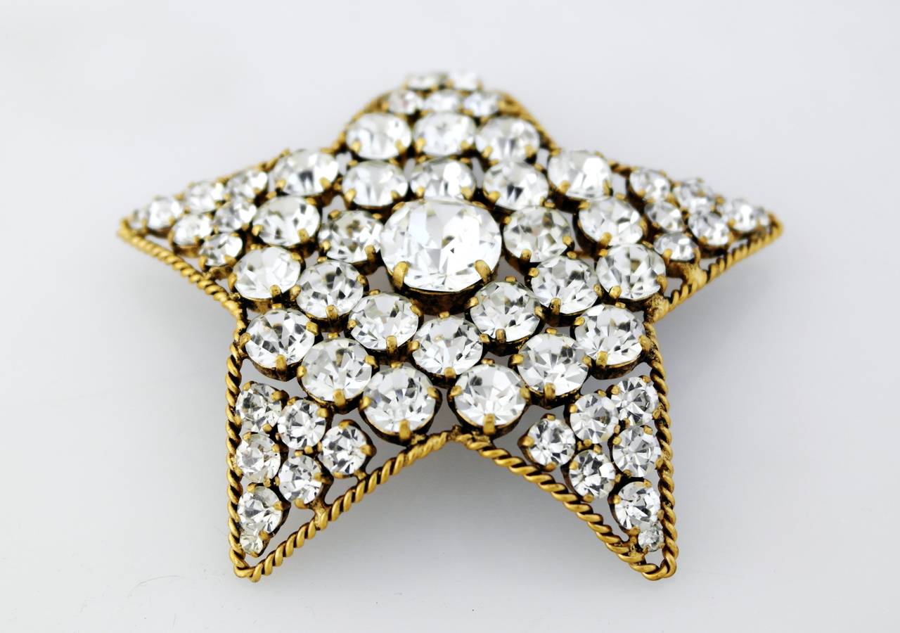 Being offered is a circa 1983 star shaped brooch/pendant made by Chanel, comprising a gold plate star decorated with many rhinestones of varying sizes, the larger one situated in the center. Please see pictures where you see the hook for the