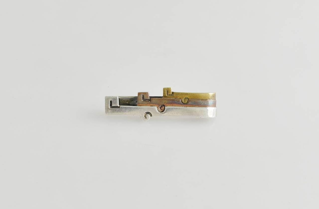 Being offered is a circa 1967 .970 silver tie clip by Antonio Pineda of Taxco, Mexico. comprising a pre Colombian motif with silver, copper and brass layers. Dimensions: 2 inches by 5/8 inches.    Marked as illustrated. In excellent