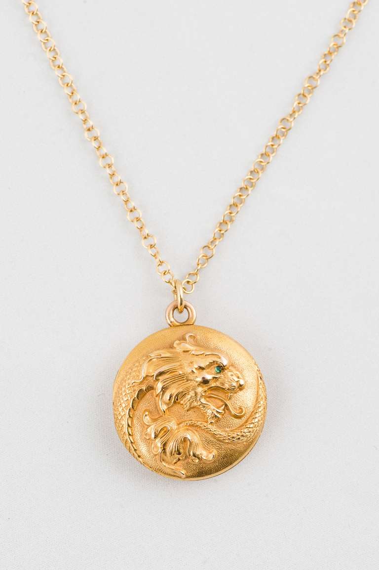 14K Yellow Gold Art Nouveau Locket, raised dragon motif has one round green emerald eye, suspended from a 22 inch, 18K yellow gold cable chain.