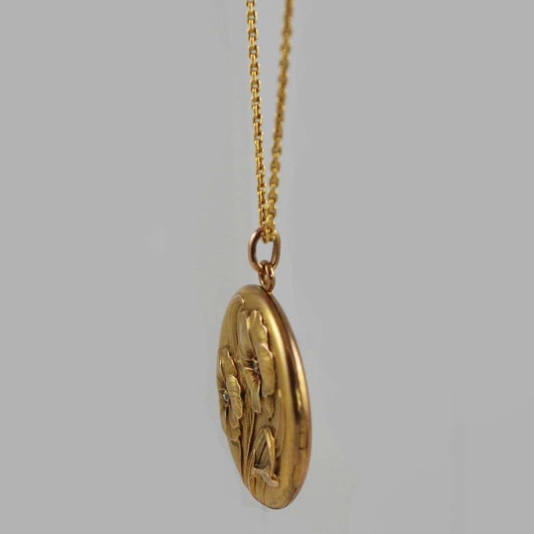 Art Nouveau 10K yellow gold locket with floral 3 dimensional relief design, with two European cut diamonds suspended from an 18k yellow gold, 22 inch cable chain.s
