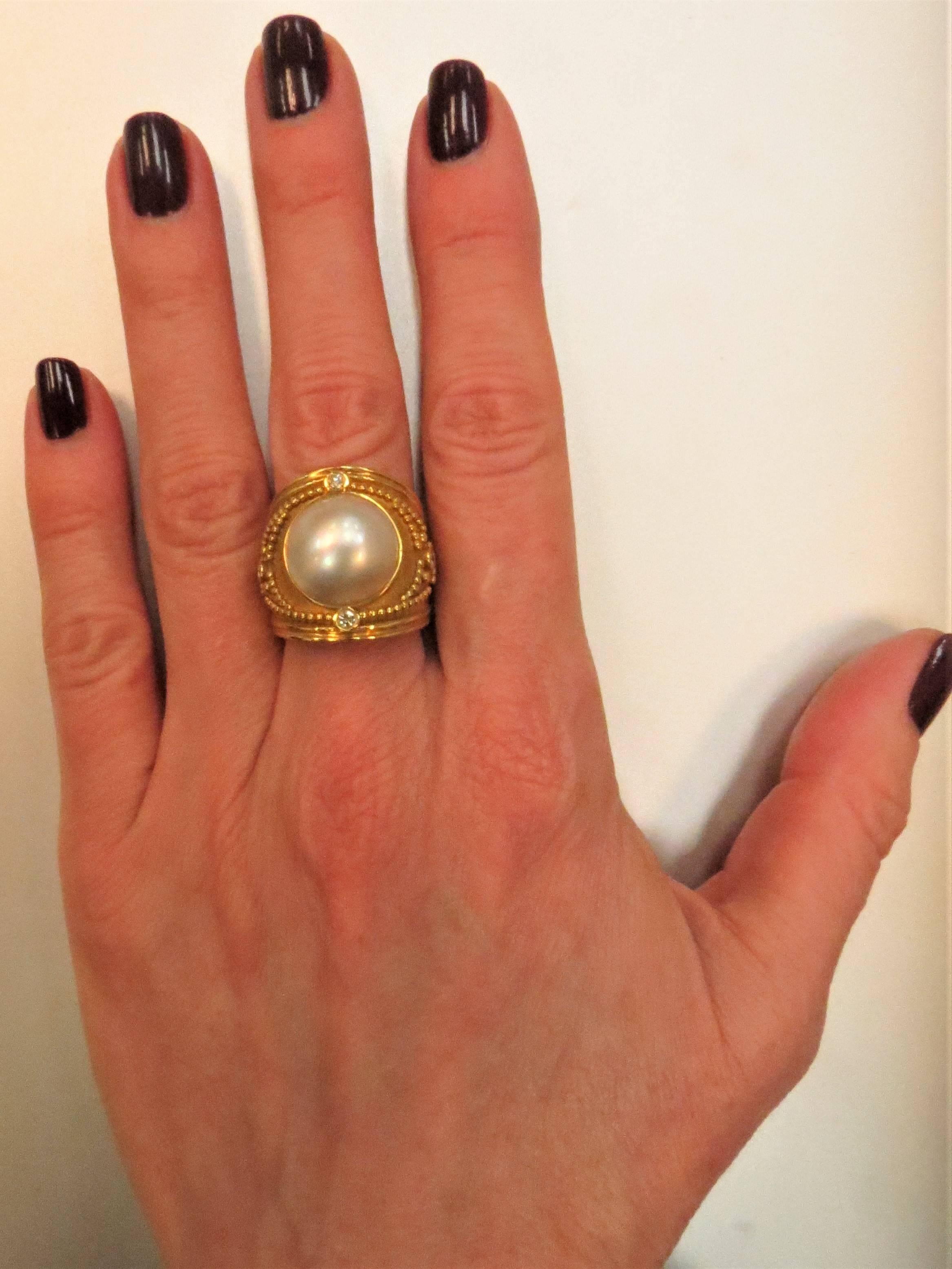 Fashionable 18K yellow gold ring, set in center with mabe pearl measuring 13mm and 4 bezel set full cut round diamonds weighing .18cts, G-H color, VS clarity.
Finger size 6. May be sized.