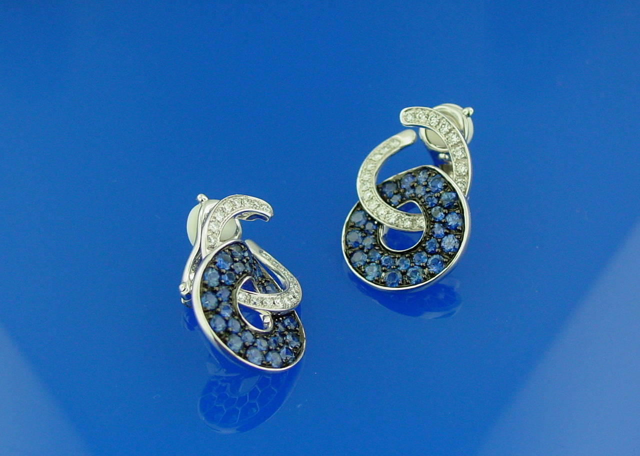 A pair of diamond and sapphire ear clips mounted in 18 karat white gold. The tops are set with round brilliant cut diamonds weighing .55 carats and the bottoms are set with round sapphires mounted in blackened gold. Hallmarked and stamped 750.