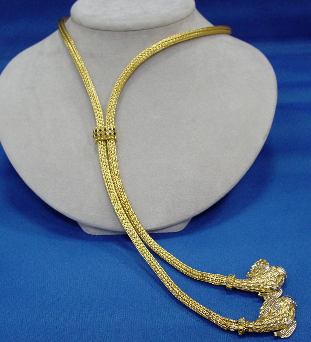 An I8 karat yellow gold braided lariat necklace by Ilias Lalaounis  terminating in two classical sea creatures studded with diamonds and emerald collars. The adjustable slide is set with two rows of sapphires and is signed Lalounis with maker's