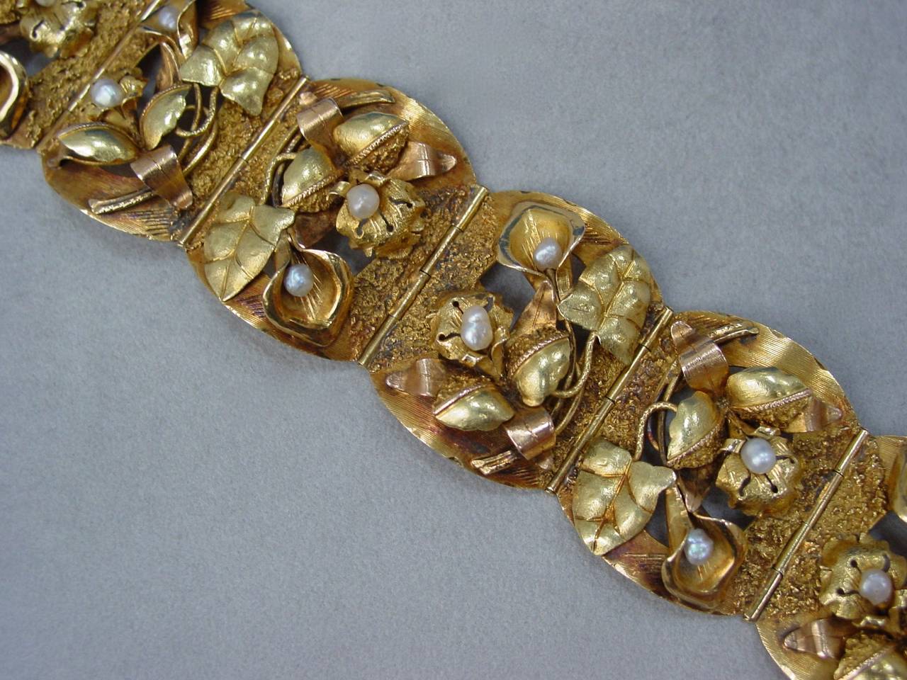 An 18 Karat gold sculpted floral bracelet, circa 1910. This beautifully patinaed  bracelet features six plaques of carved flowers with seed pearl centers in yellow and rosy gold. The bracelet measures 7 inches in length and 1.5 inches in width. 
