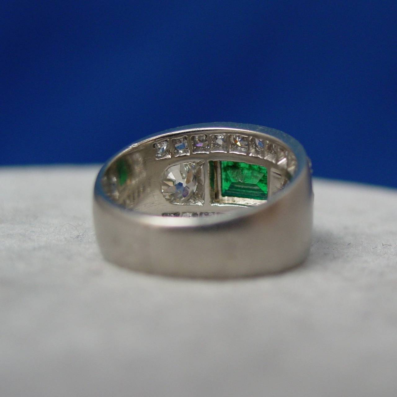 A French Art Deco Emerald and Diamond Ring, mounted in satin finished platinum. This very chic ring is set with a center rectangular cut emerald, flanked by two European cut diamonds within two rows of diamonds, also European cuts. The emerald